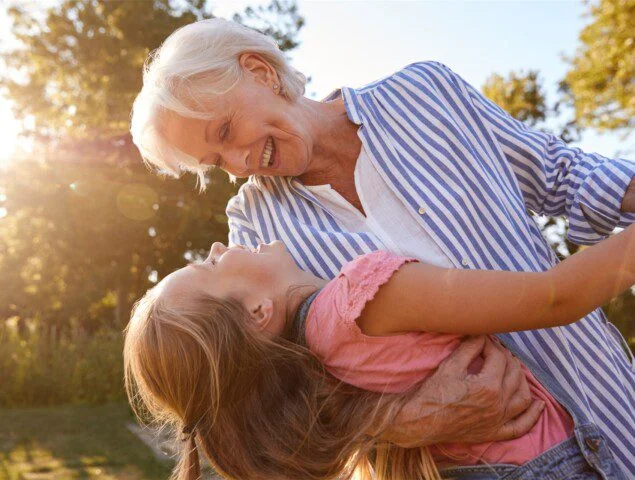 grandmother dances with her young granddaughter outdoors in the sunlight