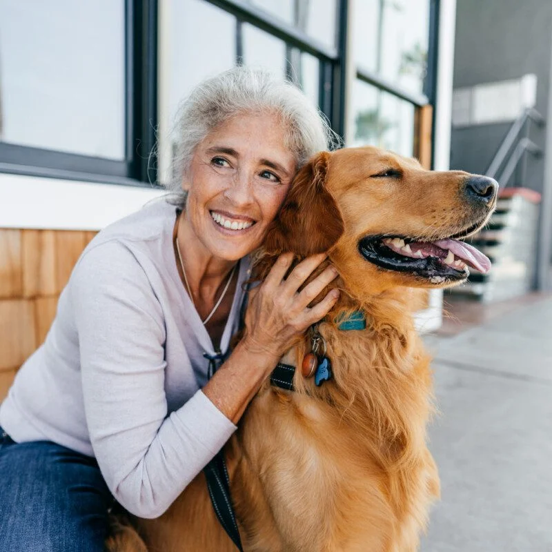 Senior woman outdoor with her best friend senior woman smiles and kneels down to pet her smiling dog