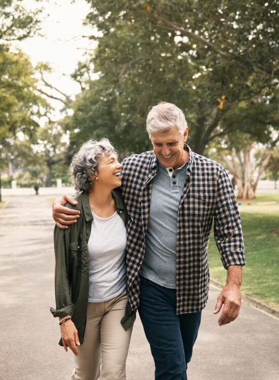 senior couple smiles and laughs together while walking arm-in-arm on a scenic path outdoors