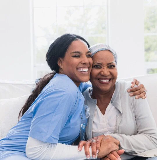seated senior woman and caregiver hug on couch, smiling