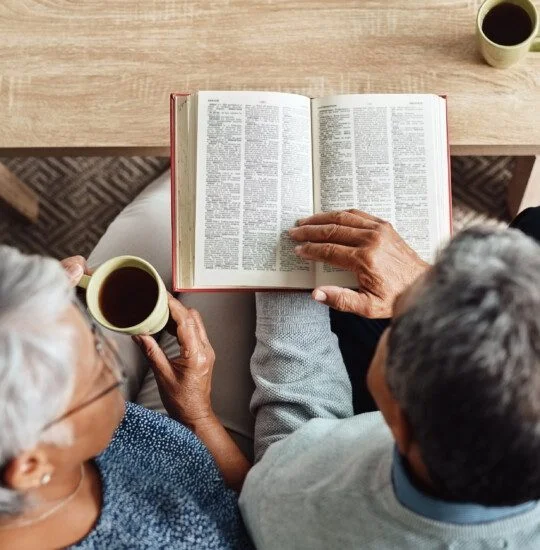 Two elderly individuals share a quiet moment with books and tea on a cozy table.