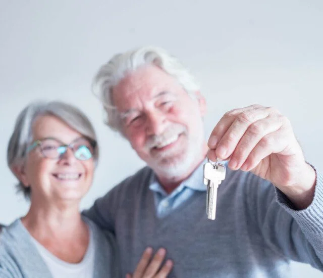 smiling senior couple holds out the keys to their new apartment