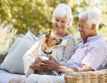 Happy senior couple sitting with a pet dog in the garden Senior couple smiles while seated on an outdoor couch, holding their dog