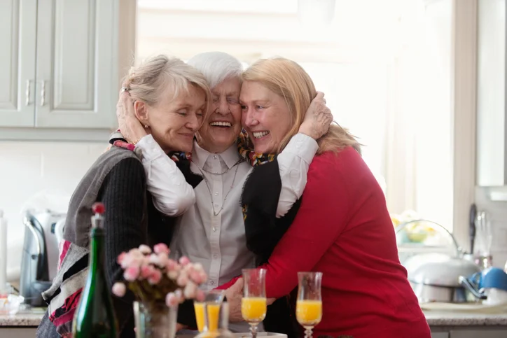 group of three senior women with mimosas smile and embrace
