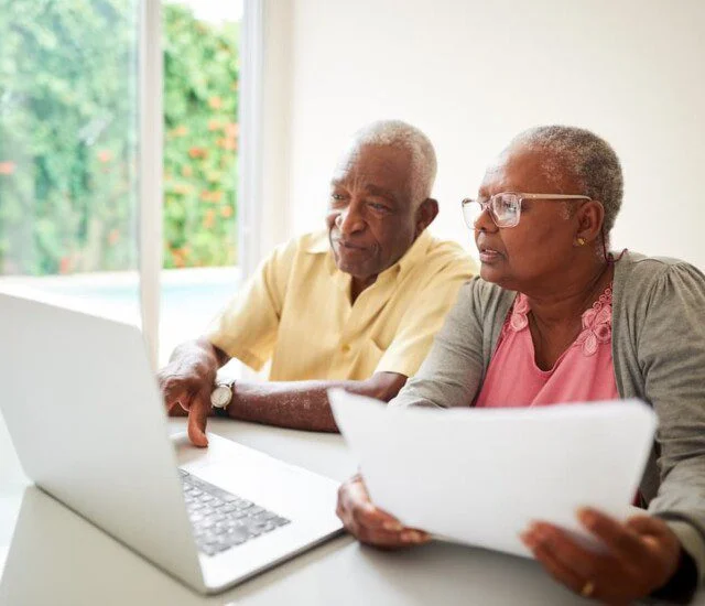 senior couple sit at a table and look at a laptop screen and documents together