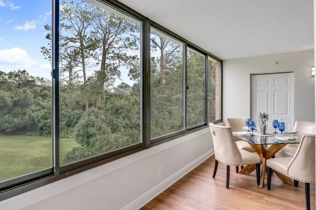 large dining room in senior villa with wall-to-wall windows featuring wooded view at Village on the Green