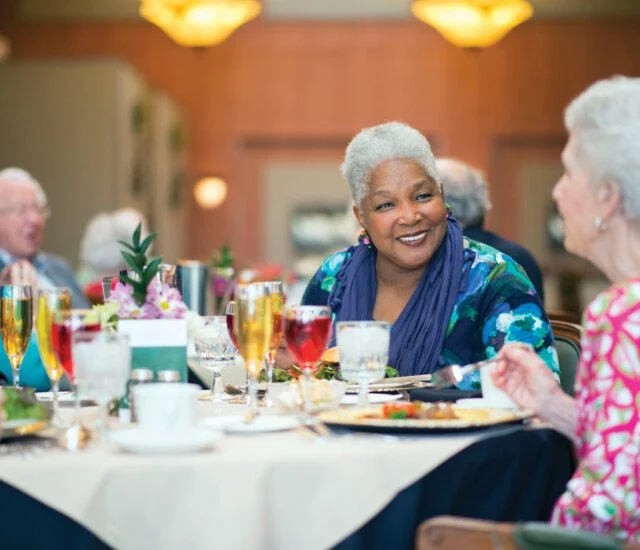 group of well-dressed senior friends enjoy an elegant dinner and drinks together at their senior living community