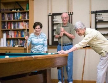 group of seniors play a game of pool together at their senior living community