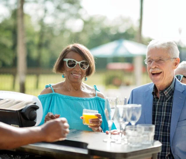 senior woman in stylish sunglasses and well-dressed senior man have cocktails at an outdoor bar at their senior living community