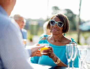 stylish senior woman in blue sunglasses accepts cocktail from bartender outdoors at her senior living community