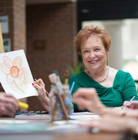 senior woman smiles and shows off her artwork to her friends during a class