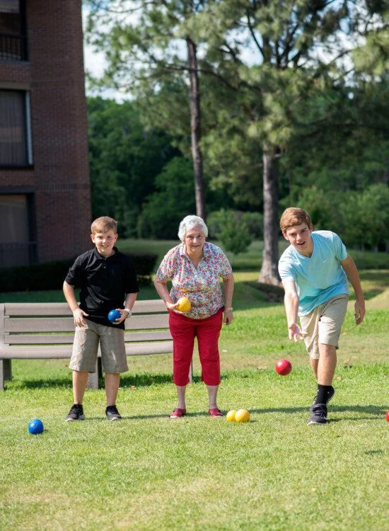 senior woman plays bocce ball with her grandsons outside of her senior living community