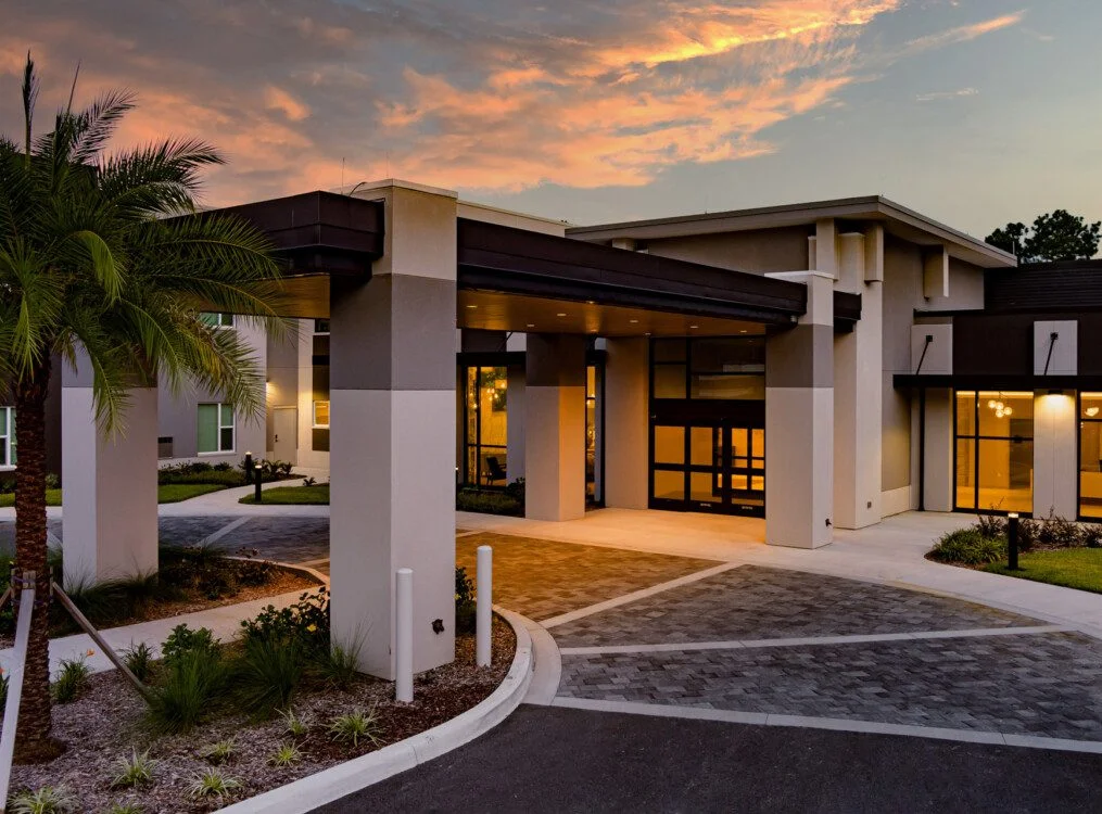 Modern building entrance at sunset with palm trees and warm lighting.