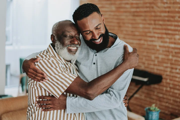 Senior father and adult son happily hugging.