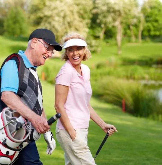 Two people smiling while walking with golf clubs on a green course.