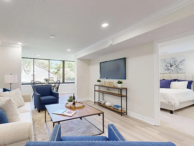Modern living room with blue accents, large window, and a view into the bedroom.