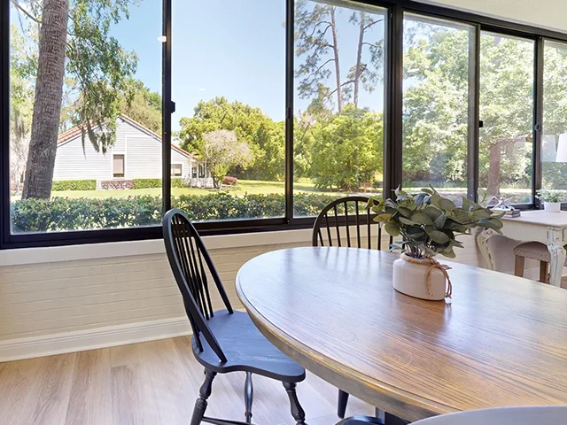 Dining area with large windows overlooking a green backyard.