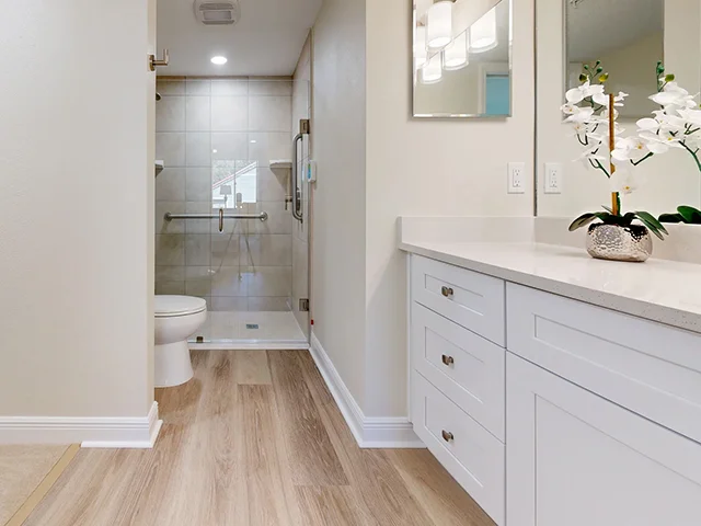 Modern bathroom with white cabinets, walk-in shower, and wood floor.