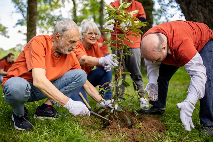 People in orange shirts planting a tree together in a park.