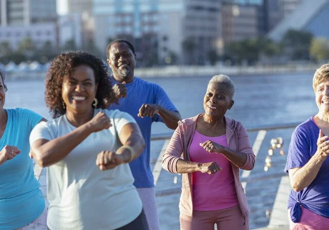 Group of diverse seniors exercising outdoors by the waterfront, smiling and active.