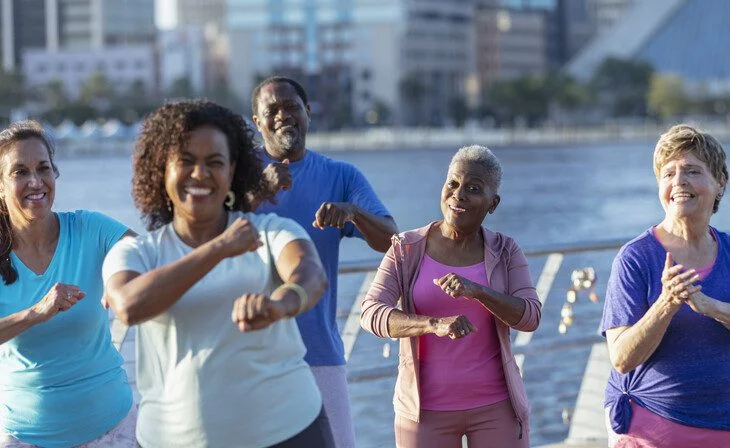 Group of diverse seniors exercising outdoors by the waterfront, smiling and active.