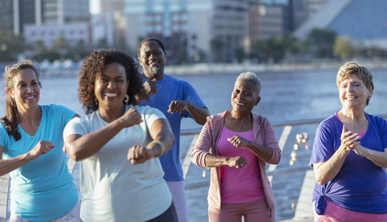 Group of diverse seniors exercising outdoors by the waterfront, smiling and active.