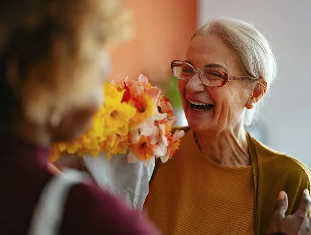 Smiling elderly woman receives a bouquet of flowers indoors.