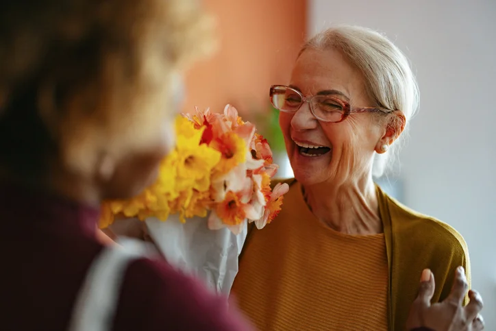 Smiling elderly woman receives a bouquet of flowers indoors.