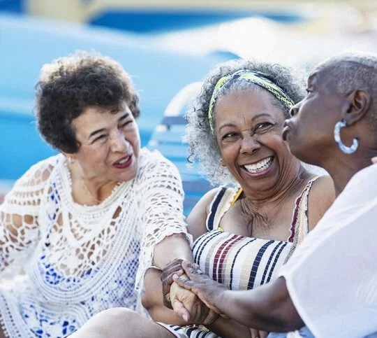 Three women sitting and smiling together outdoors.