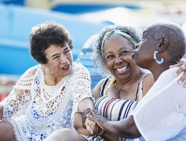 Three women sitting and smiling together outdoors.