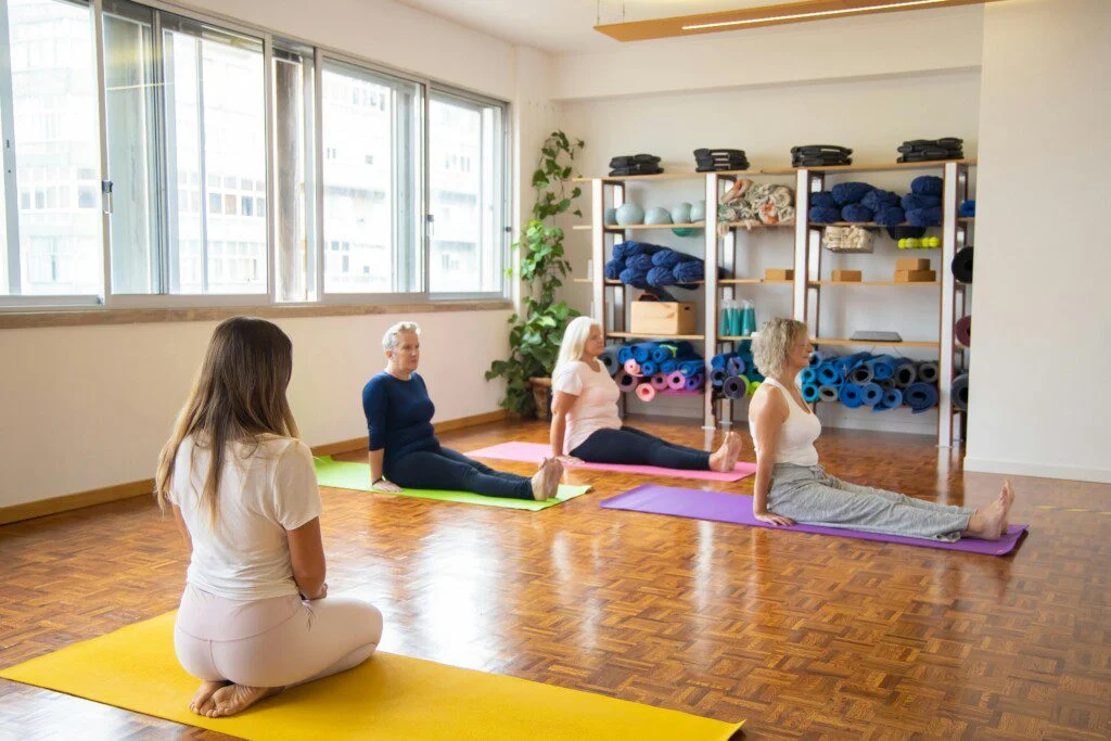 People practicing yoga in a bright studio with colorful mats and shelves of equipment.