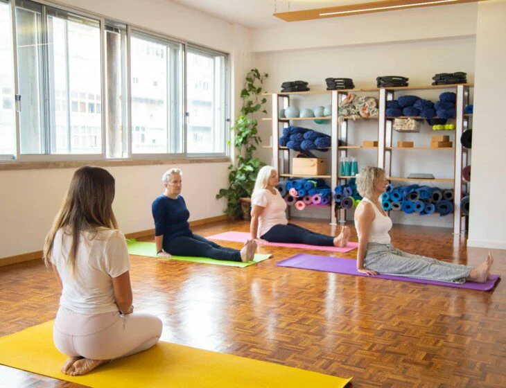 People practicing yoga in a bright studio with colorful mats and shelves of equipment.