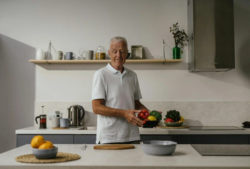 Senior holding a bowl of vegetables in a modern kitchen.