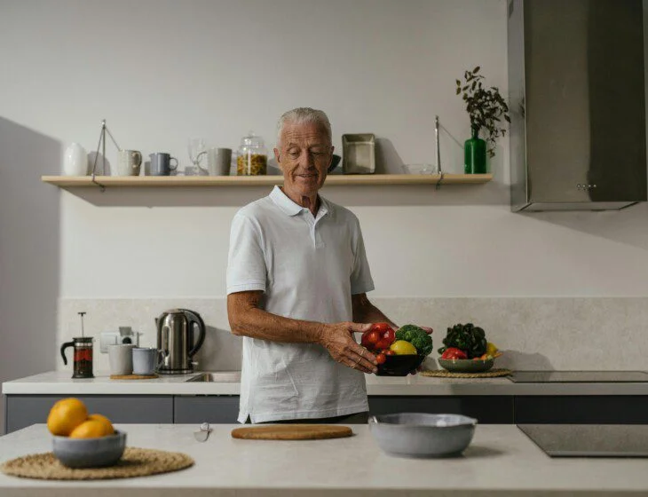 Senior holding a bowl of vegetables in a modern kitchen.