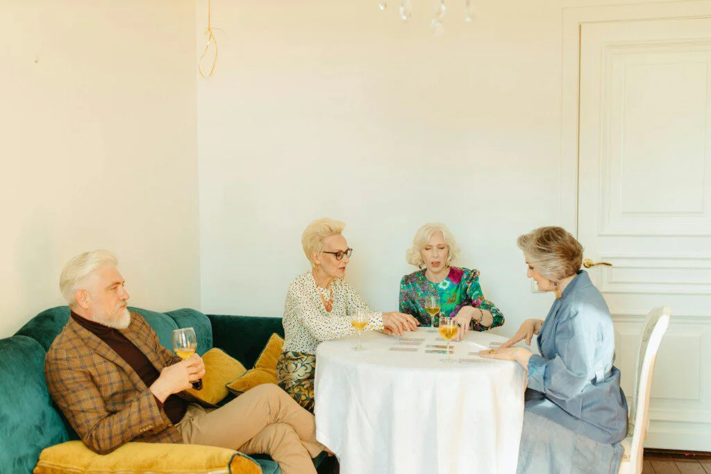 Four people playing cards at a table with drinks in a cozy room.