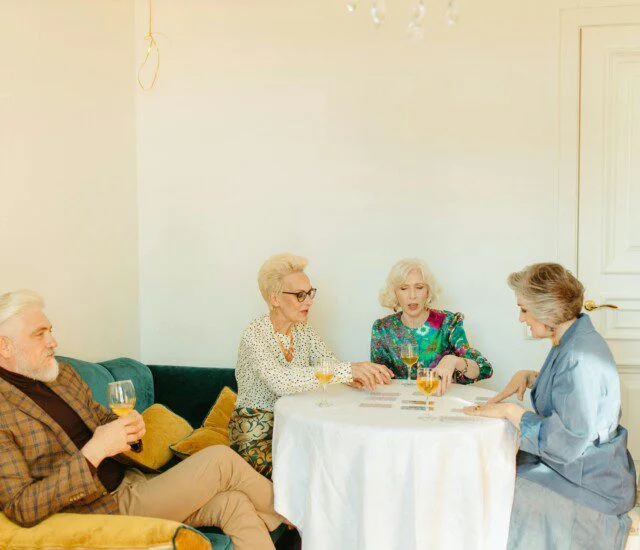 Four people playing cards at a table with drinks in a cozy room.