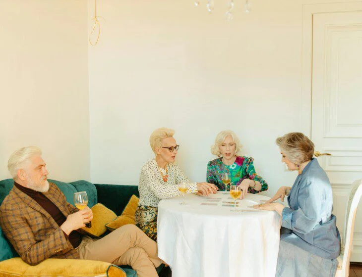 Four people playing cards at a table with drinks in a cozy room.