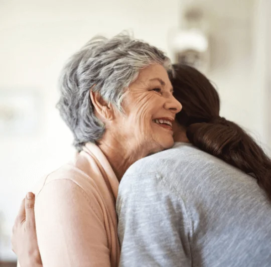 Elderly woman warmly embraces a younger person indoors.