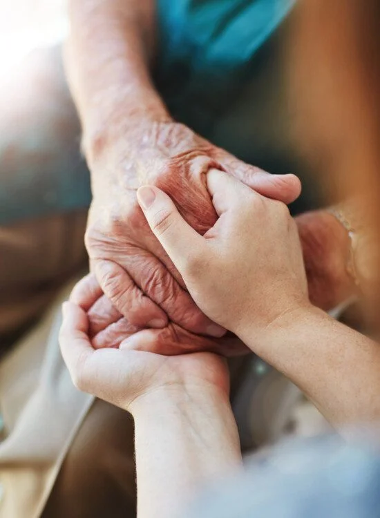 Hands of a young person holding an elderly person's hand compassionately.