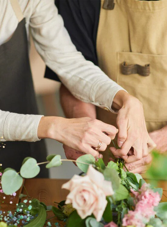Hands arranging flowers on a table, with roses and eucalyptus leaves.