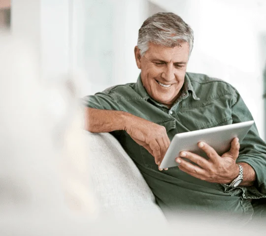 Man smiling while using a tablet on a couch.