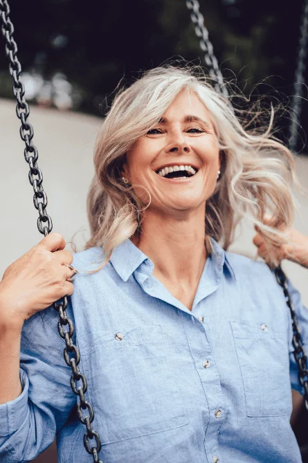 Smiling woman on a swing in a blue shirt outdoors.