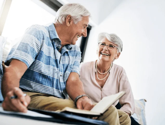Elderly couple laughing and writing in a notebook together indoors.