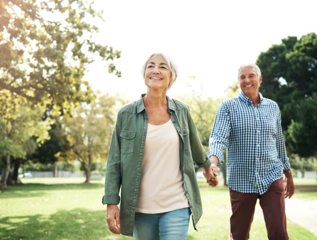 Smiling couple walks hand in hand through a sunny park.