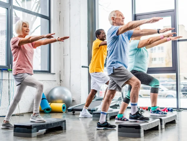 Seniors exercising in a gym class with step platforms.