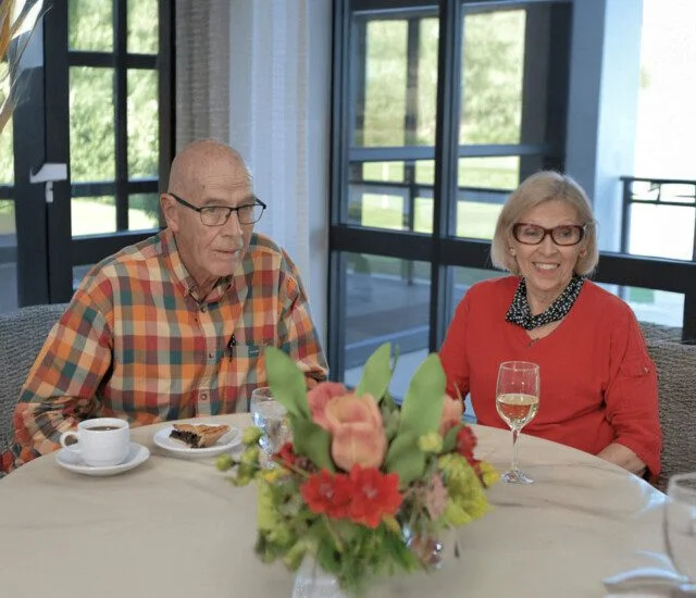 Elderly couple enjoying drinks at a table with bright floral centerpiece.