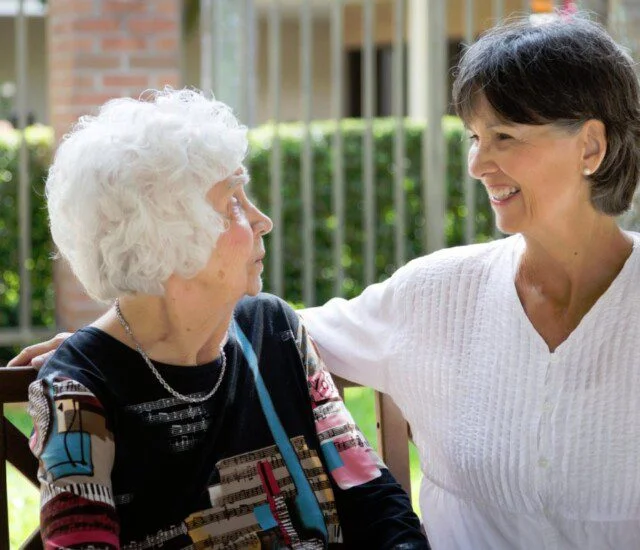 Two women sitting outside, smiling and talking to each other on a sunny day.
