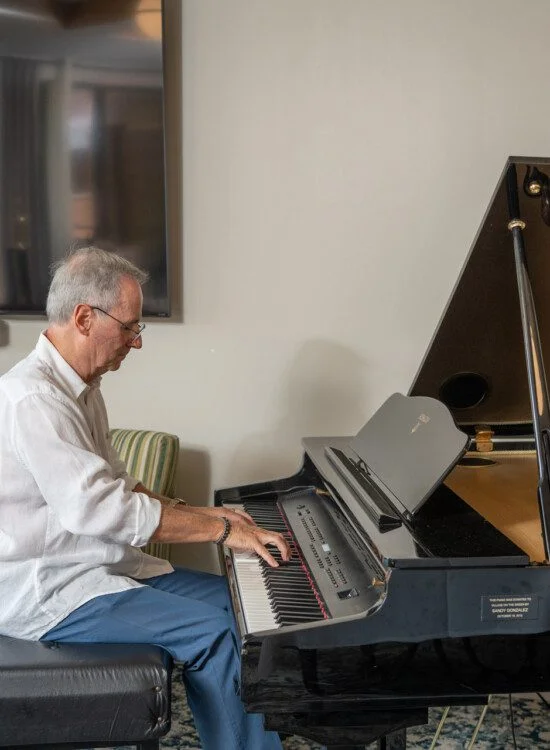 Man in white shirt playing a grand piano in a living room.
