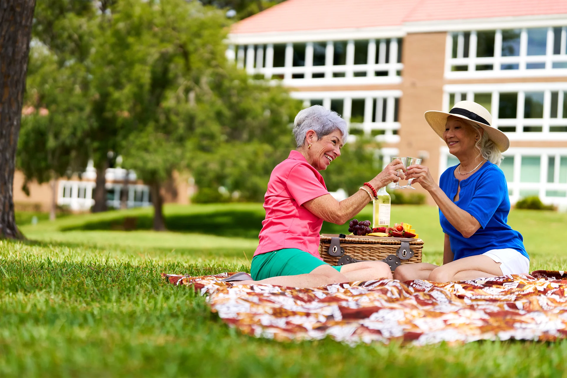 Two women enjoy a picnic on grass with food and drinks.