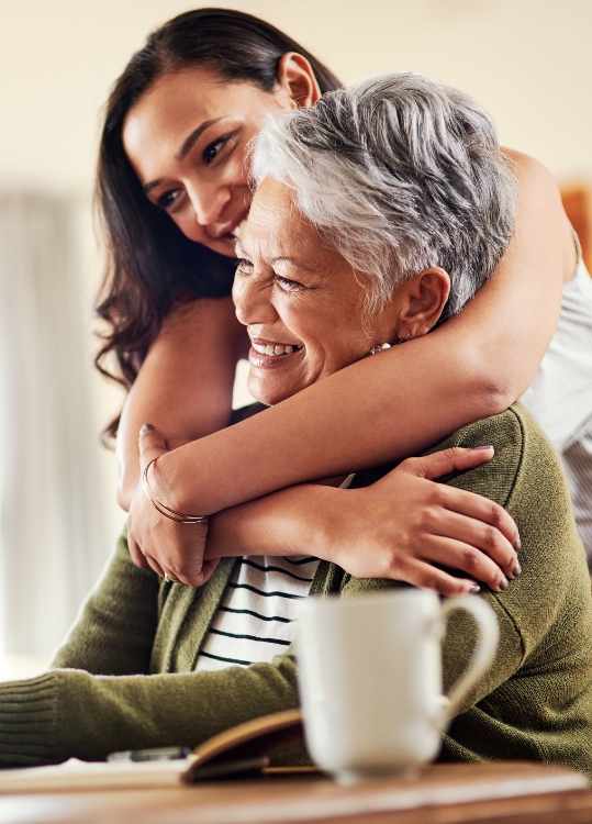 adult daughter hugs senior mother from behind